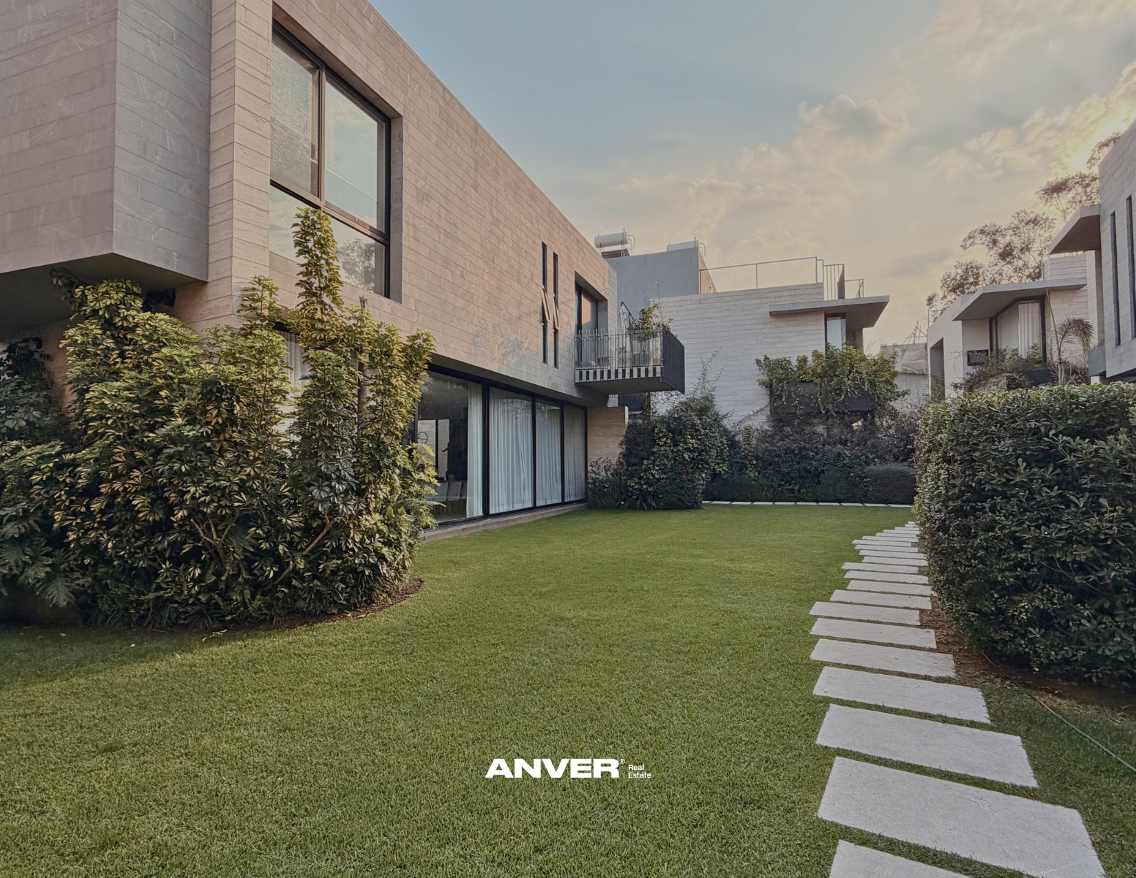Vista de casas modernas con jardines, sendero de piedra en césped, cielo nublado, en un vecindario residencial.
