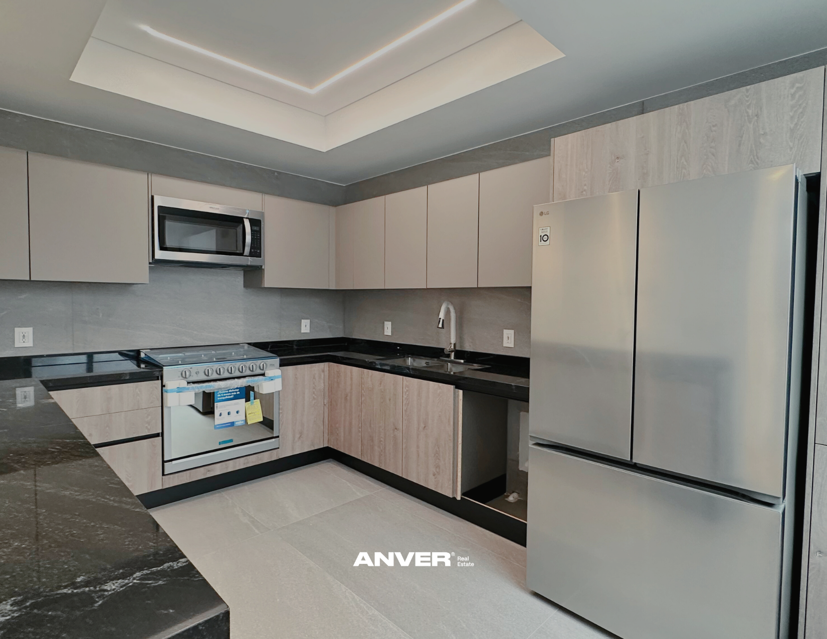 Cocina moderna con gabinetes beige, electrodomésticos de acero inoxidable, granito negro en encimeras, y un techo con iluminación empotrada.
