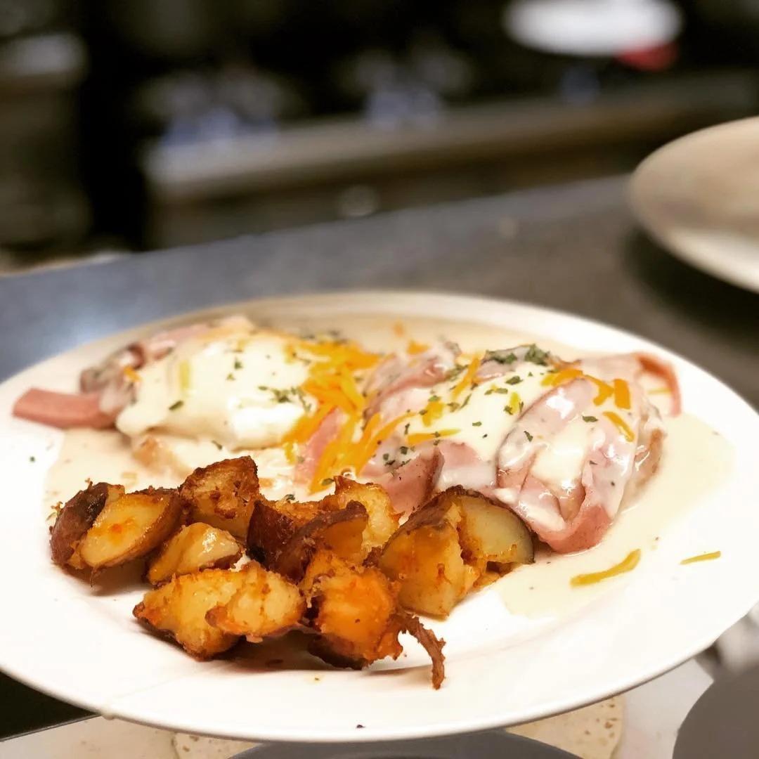 Plate with fried potatoes, baked ham topped with melted cheese and eggs, garnished with herbs.