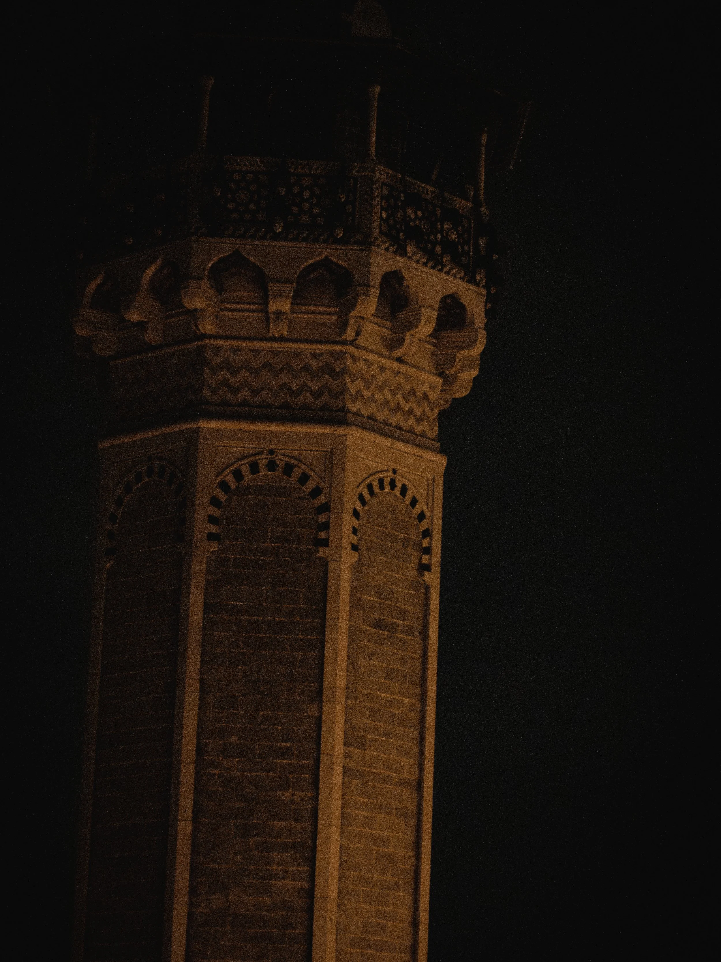 Nighttime photo of a clock tower with intricate architectural details, partially illuminated against a dark sky.