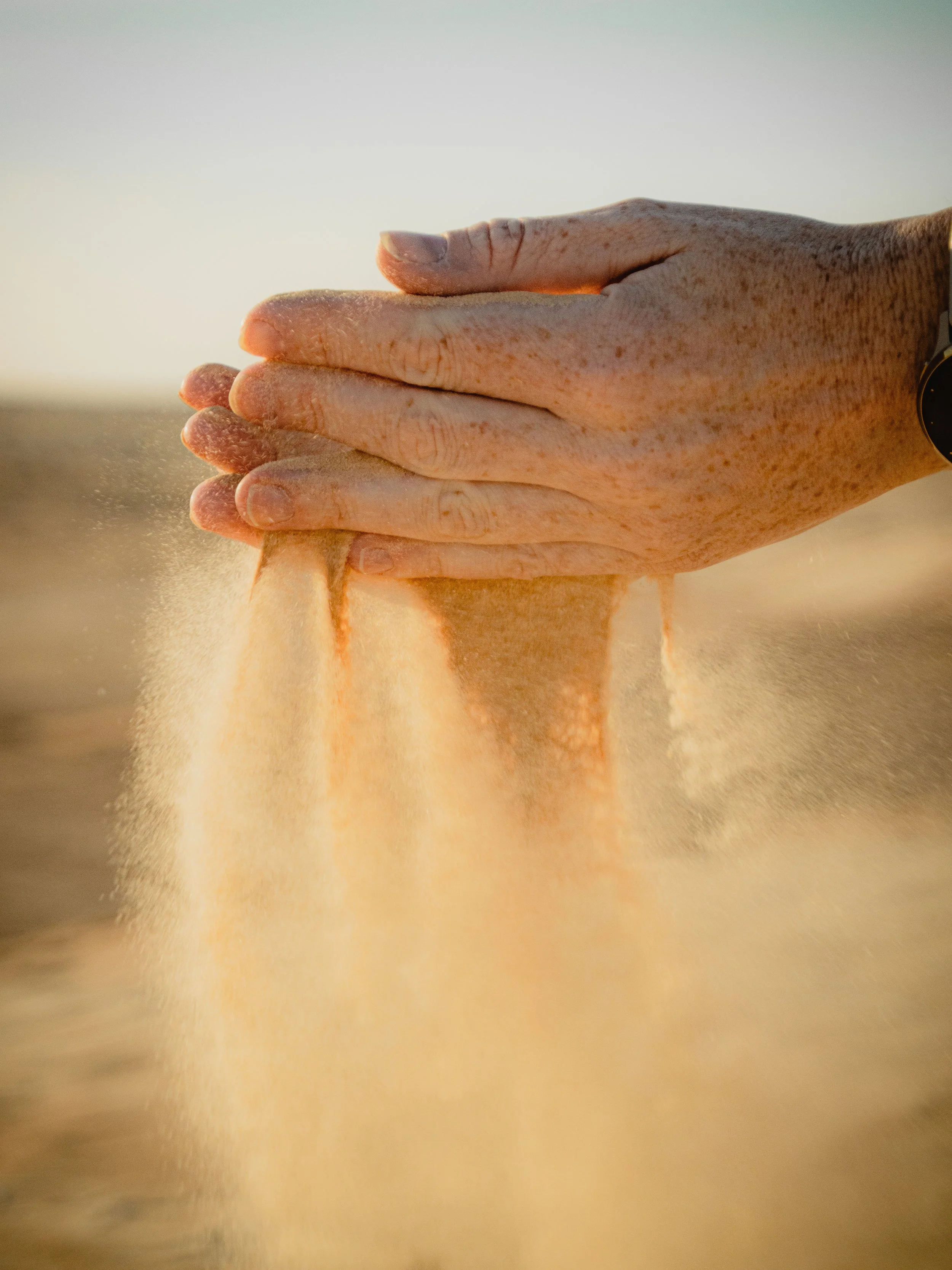 A close-up of a hand with light skin and freckles, dusted with flour, pressing down on a surface with more flour, possibly preparing dough.