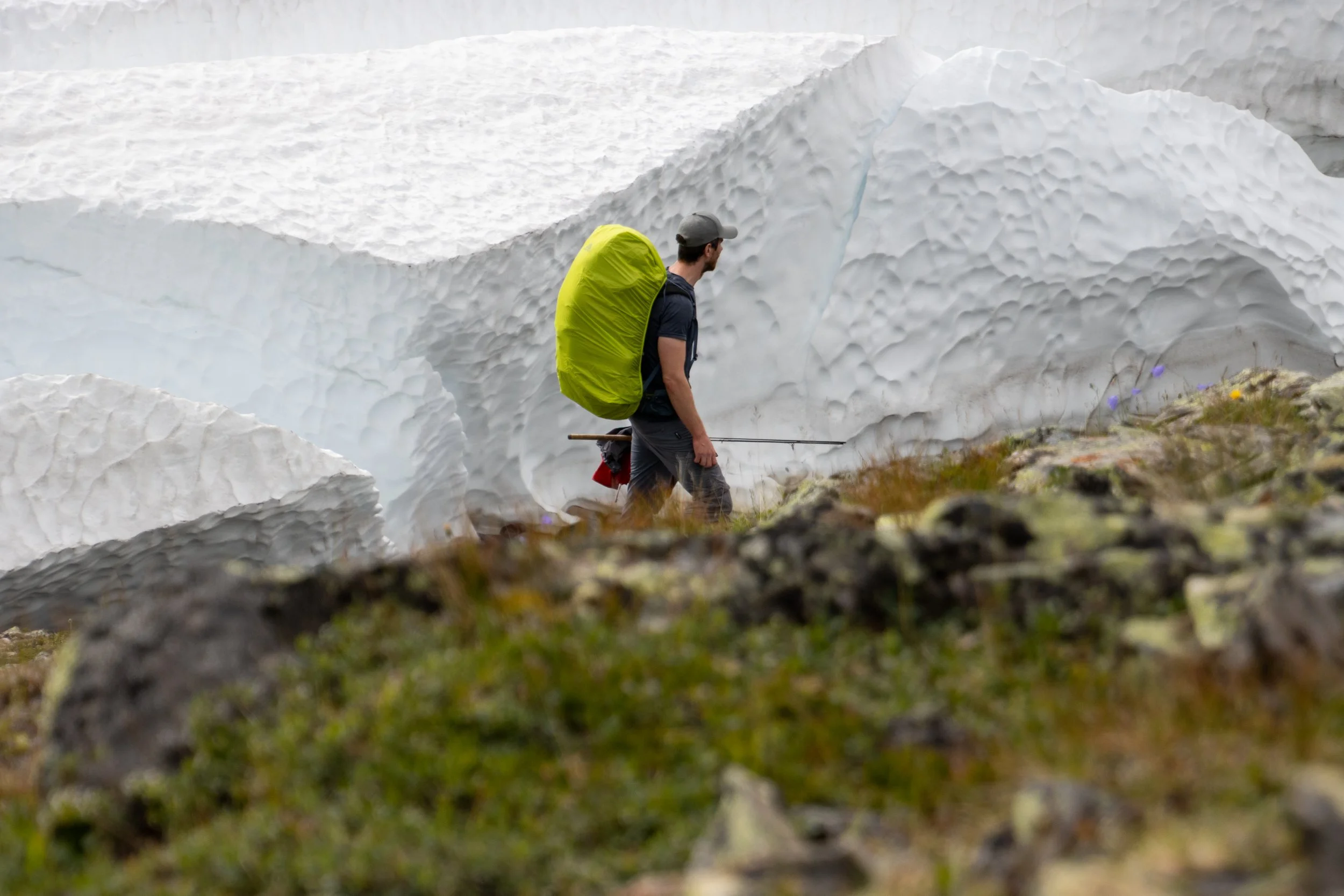 A man with a backpack walking through snow and ice in a mountainous area.