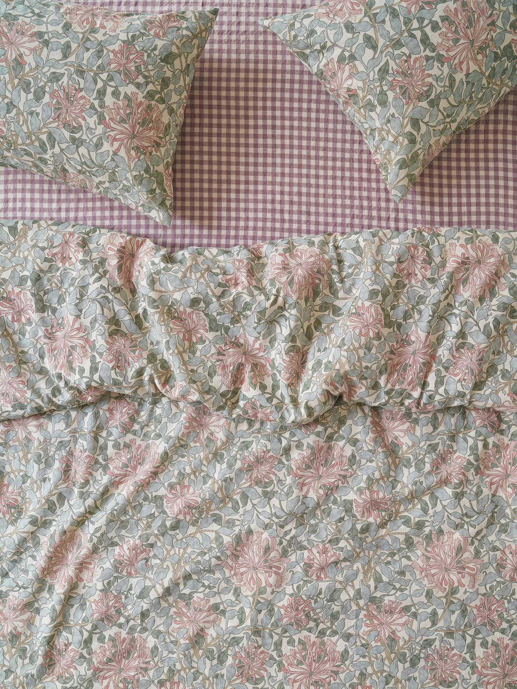 A bed with a floral patterned comforter and matching pillowcases on a pink and white gingham bedspread.