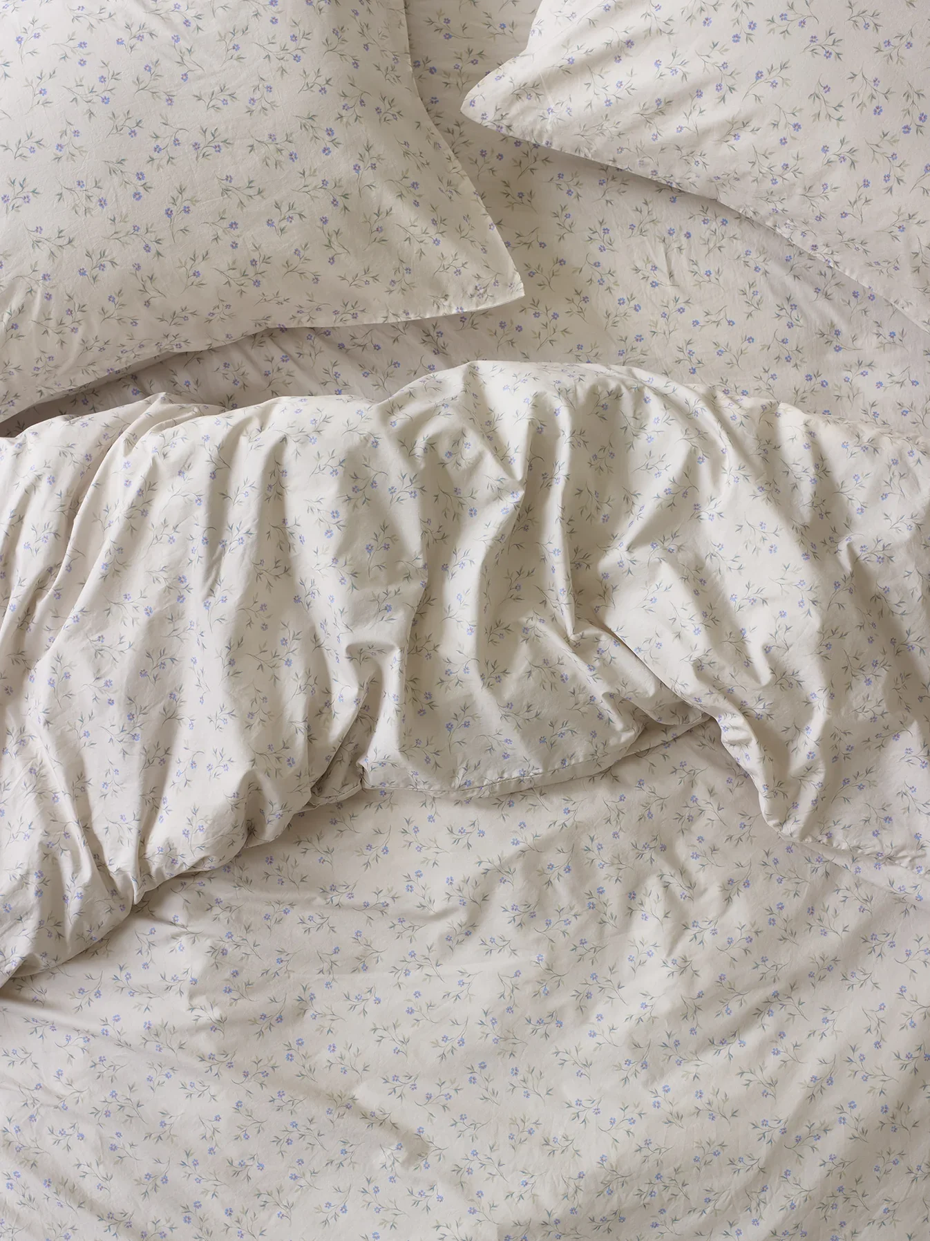 Close-up of a bed with cream-colored sheets and pillowcases that have a delicate floral pattern with small purple flowers and green leaves.