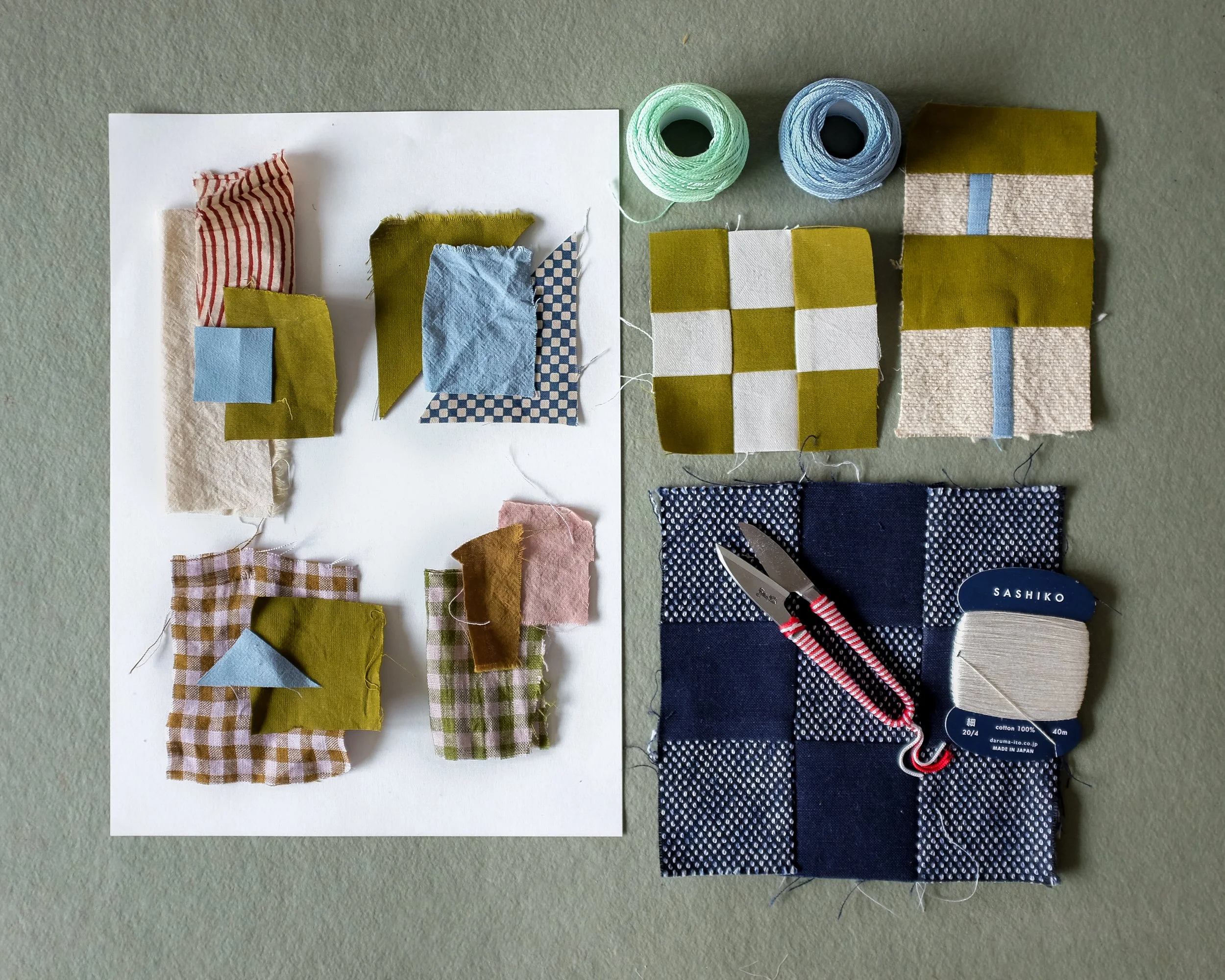 Various fabric pieces, spools of thread, scissors, and a pin cushion arranged on a table, suggesting a sewing or craft project.