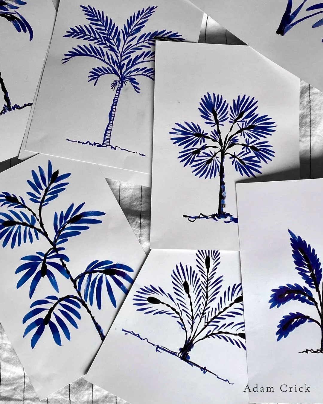 Multiple art prints of palm and tree branches in blue, black, and white, arranged on a surface.
