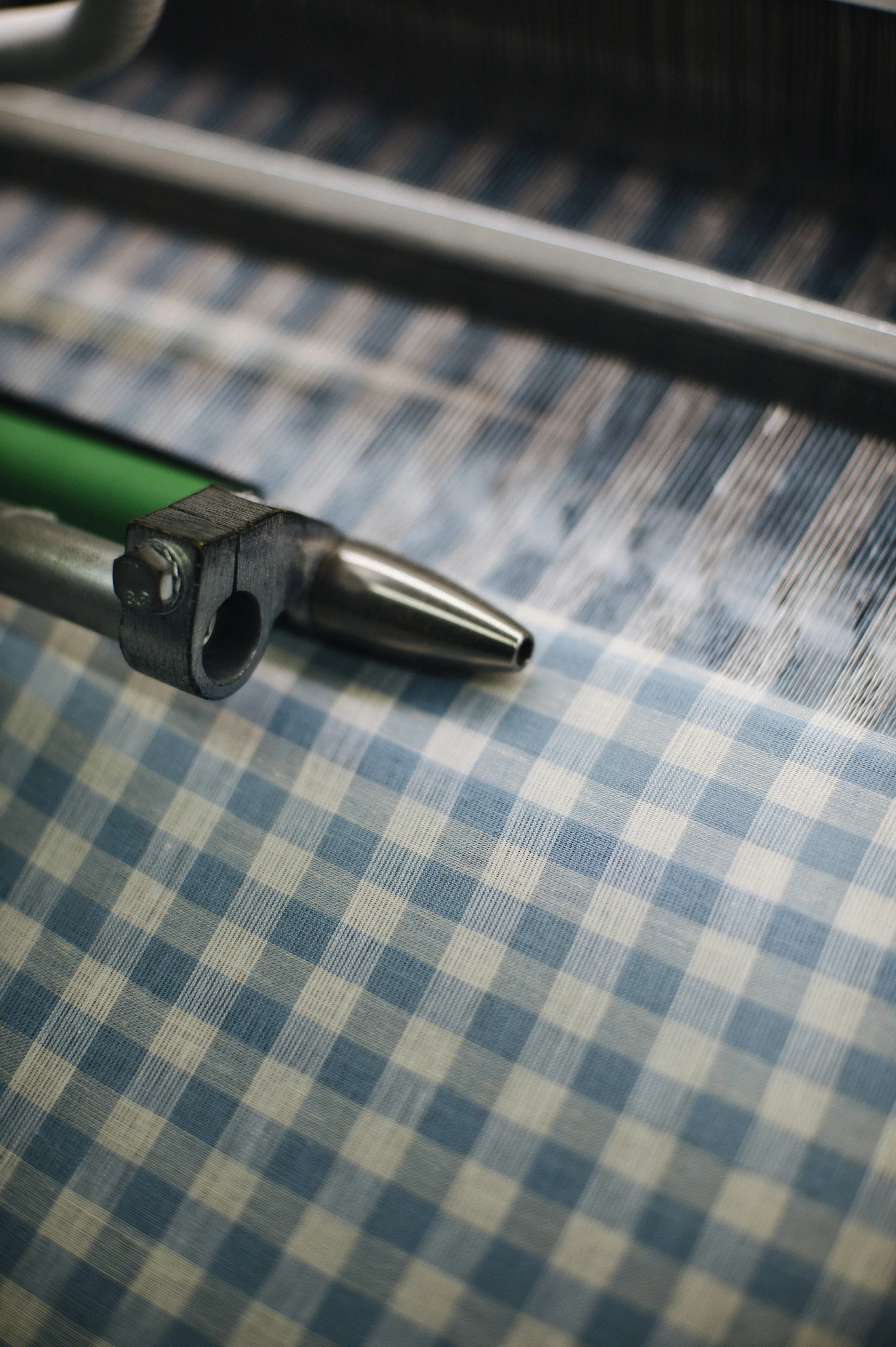 Close-up of fabric with a blue and beige checkered pattern, with a metal and green wooden frame crossing the fabric.
