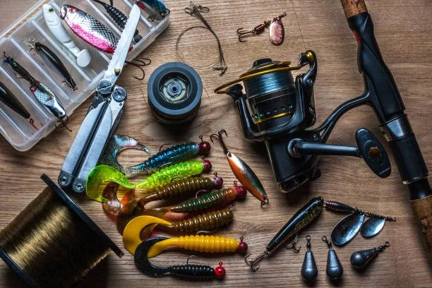 Fishing tackle including lures, hooks, a spinning reel, a fishing rod, and fishing accessories on a wooden surface.