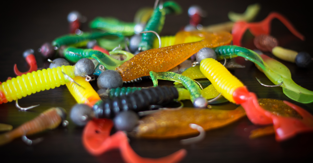Assorted colorful fishing lures and artificial bait on a dark surface.