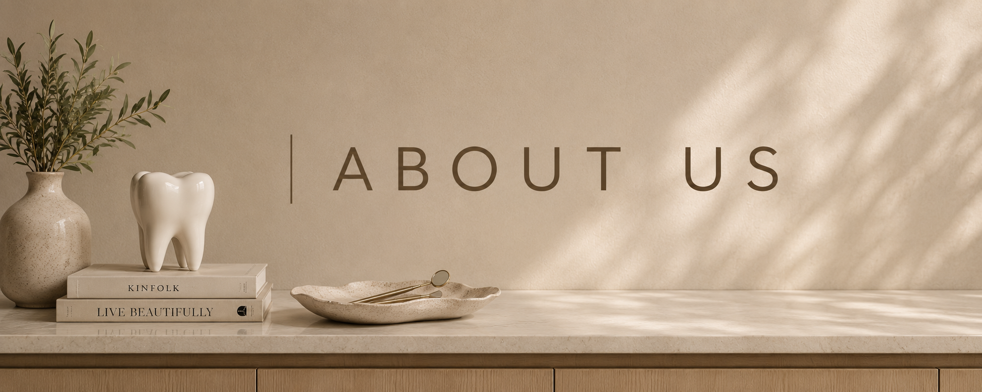 A beige interior scene with a marble countertop, a tall vase with green leaves, a ceramic tooth sculpture, stacked books titled "Kinfolk" and "Live Beautifully," a decorative tray with small mirrors, and the words "About Us" on the wall.