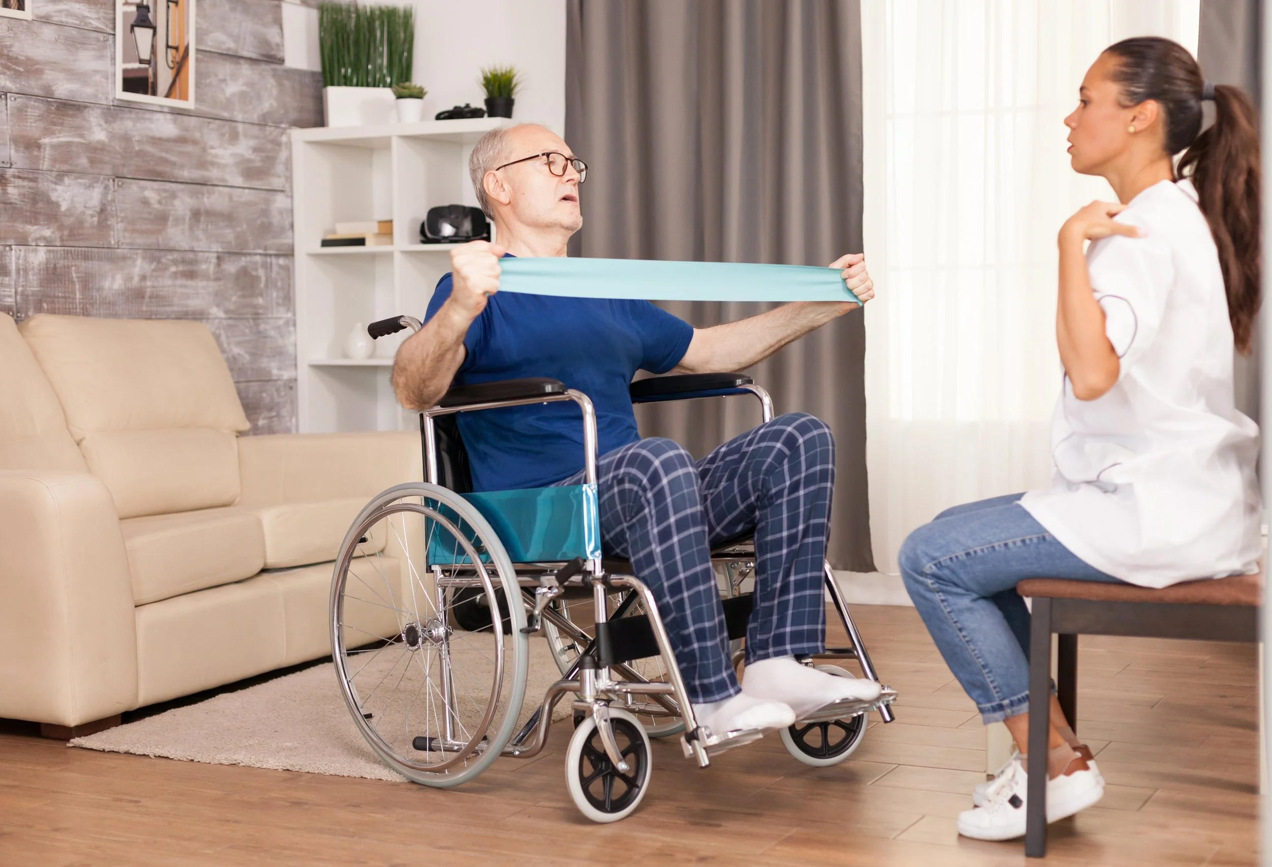 An elderly man in a wheelchair resisting a physical therapist's shoulder massage.