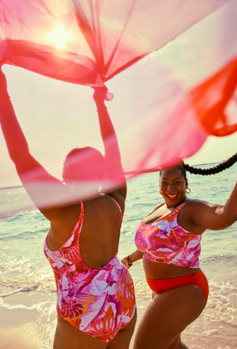 Two women enjoying a day at the beach, holding a pink umbrella and smiling.