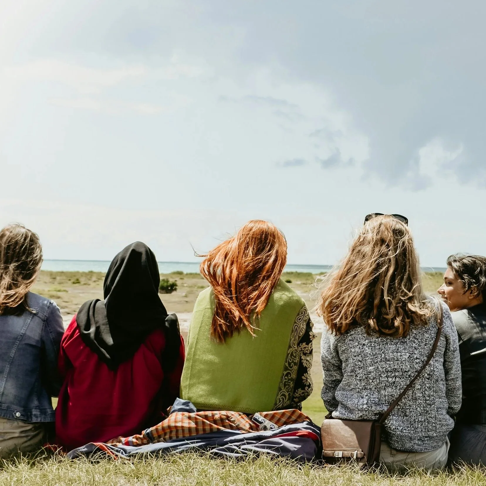 A diverse group of women sitting together outdoors by the water enjoying a group celebration