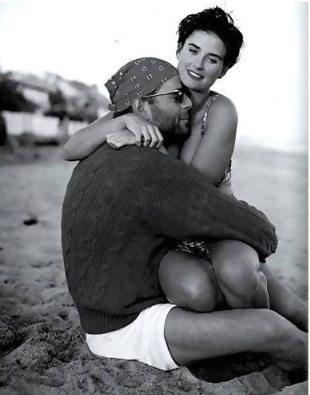 Un couple assis sur la plage, en train de se faire un câlin et de sourire, en noir et blanc.