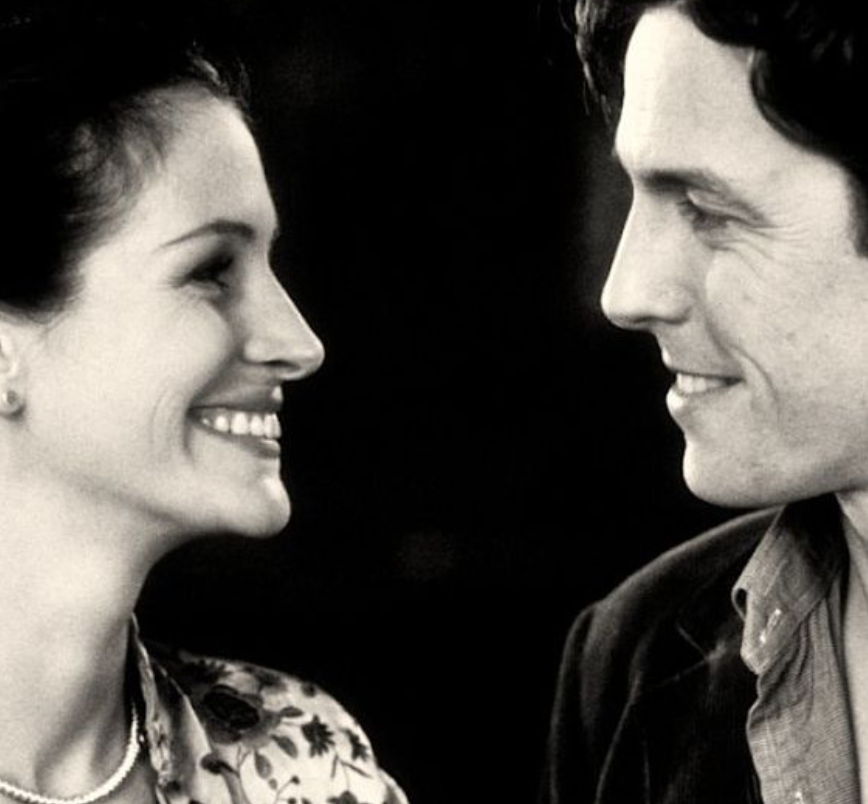 Deux personnes, un homme et une femme, se regardent en souriant, dans une ambiance chaleureuse, noir et blanc.