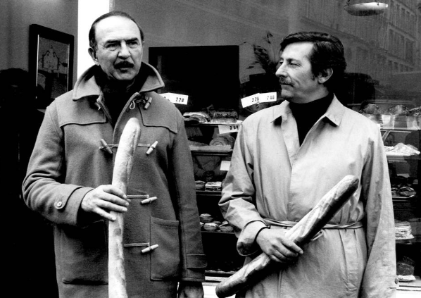 Deux hommes dans une boutique, chacun tenant une baguette de pain.