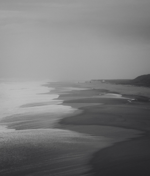 Plage avec sable humide et vagues, horizon lointain, ciel nuageux, environnement calme.