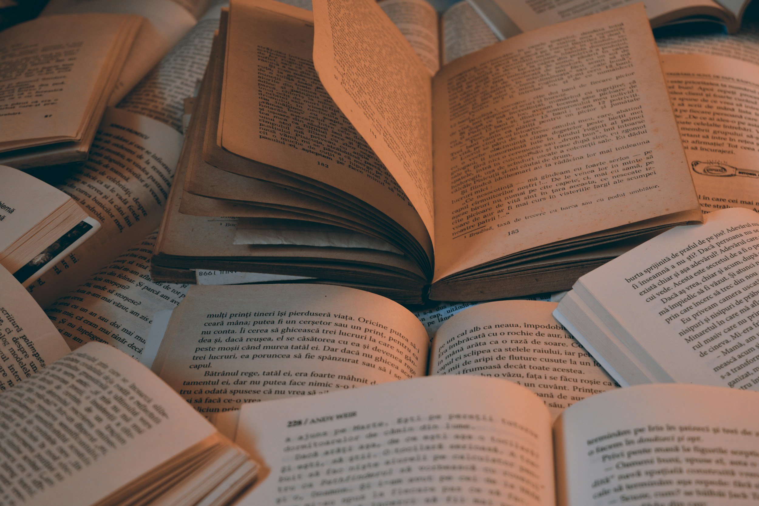 Multiple open and closed books scattered overlapping on a surface, with one open book prominently in the center of the image.