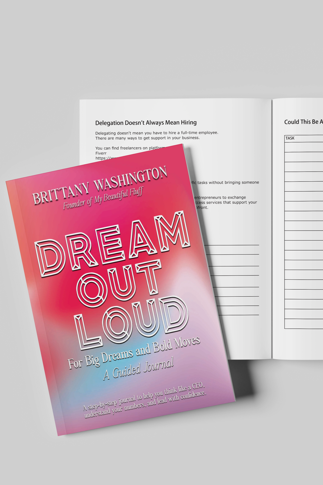 A product mockup displaying a closed journal resting on top of an open page spread, set against a plain grey background.

The closed journal on the left has a pink and purple gradient cover. At the top, it reads "BRITTANY WASHINGTON, Founder of My Be