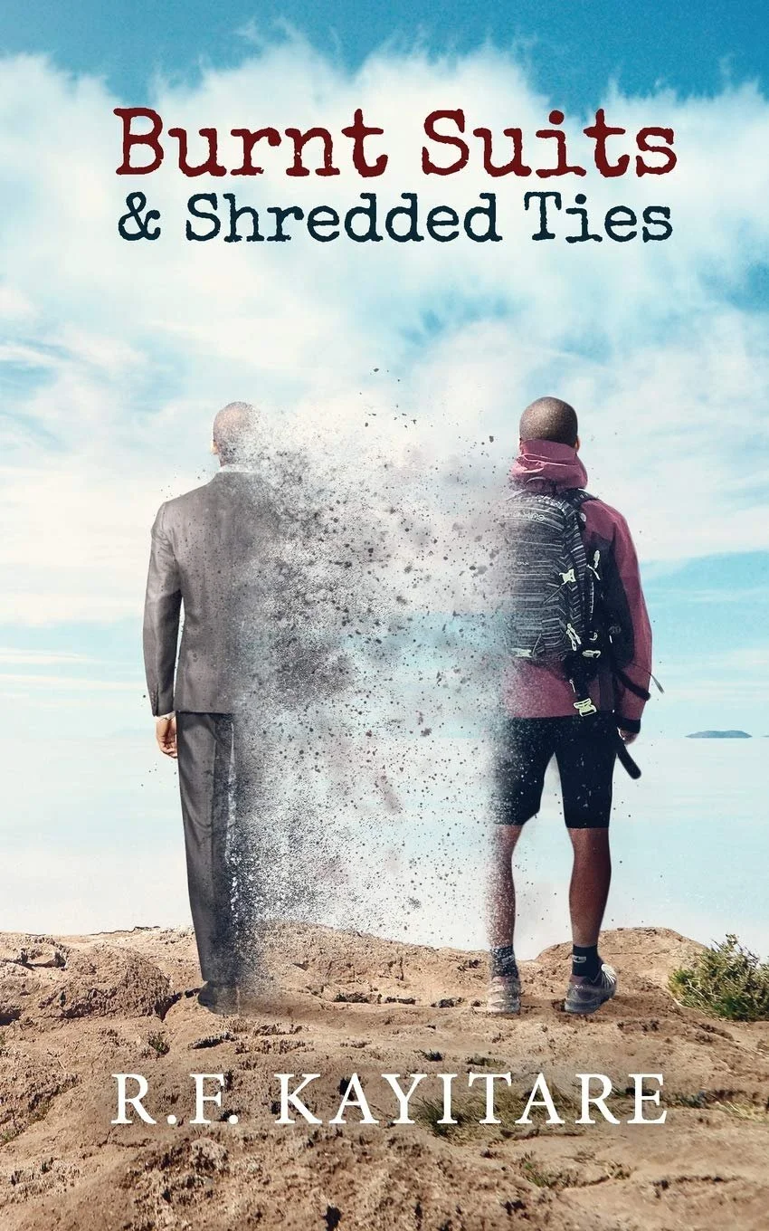 Book cover titled "Burnt Suits & Shredded Ties" by R.F. Kayitare, showing a person in a business suit and a person with outdoor gear on a cliff edge with the ocean behind them, one figure disintegrating into dust.