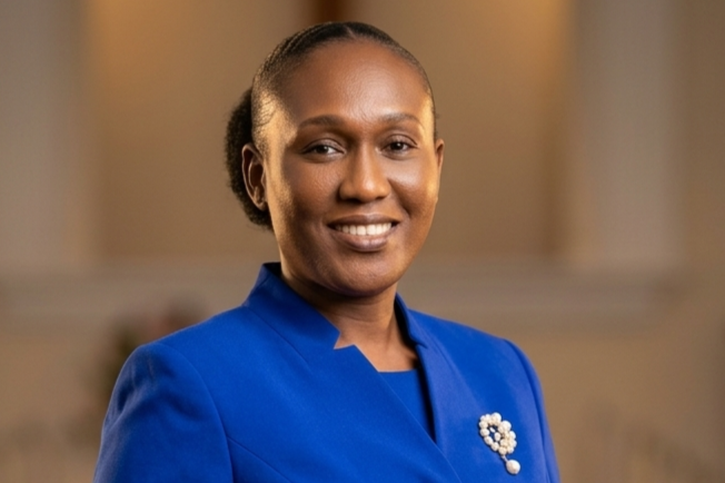Professional portrait of a smiling woman wearing a royal blue suit, standing with folded hands inside a church sanctuary with softly blurred pews and warm lighting in the background.