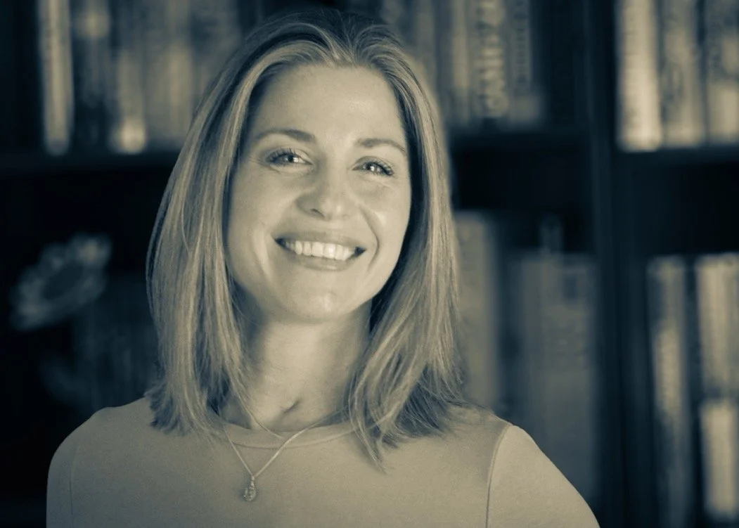 A woman with shoulder-length hair smiling in front of a bookshelf.