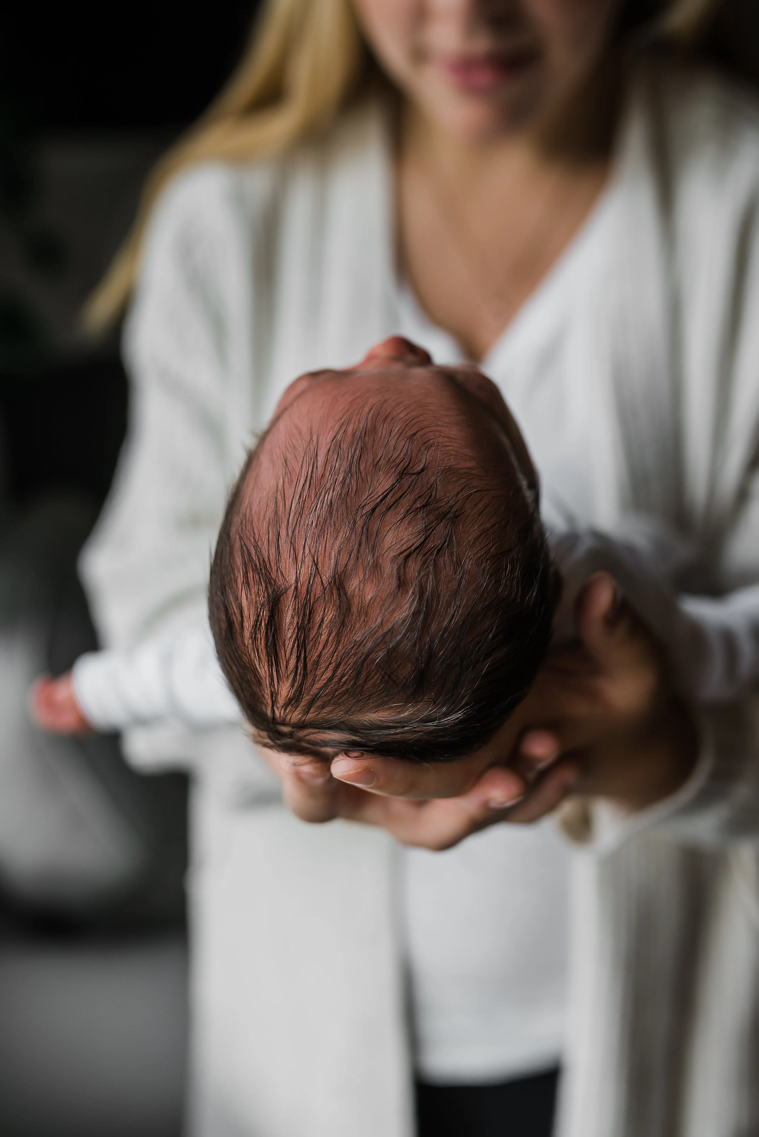 A woman holding a baby's head, with the focus on the baby's hair and the woman's partial face visible.