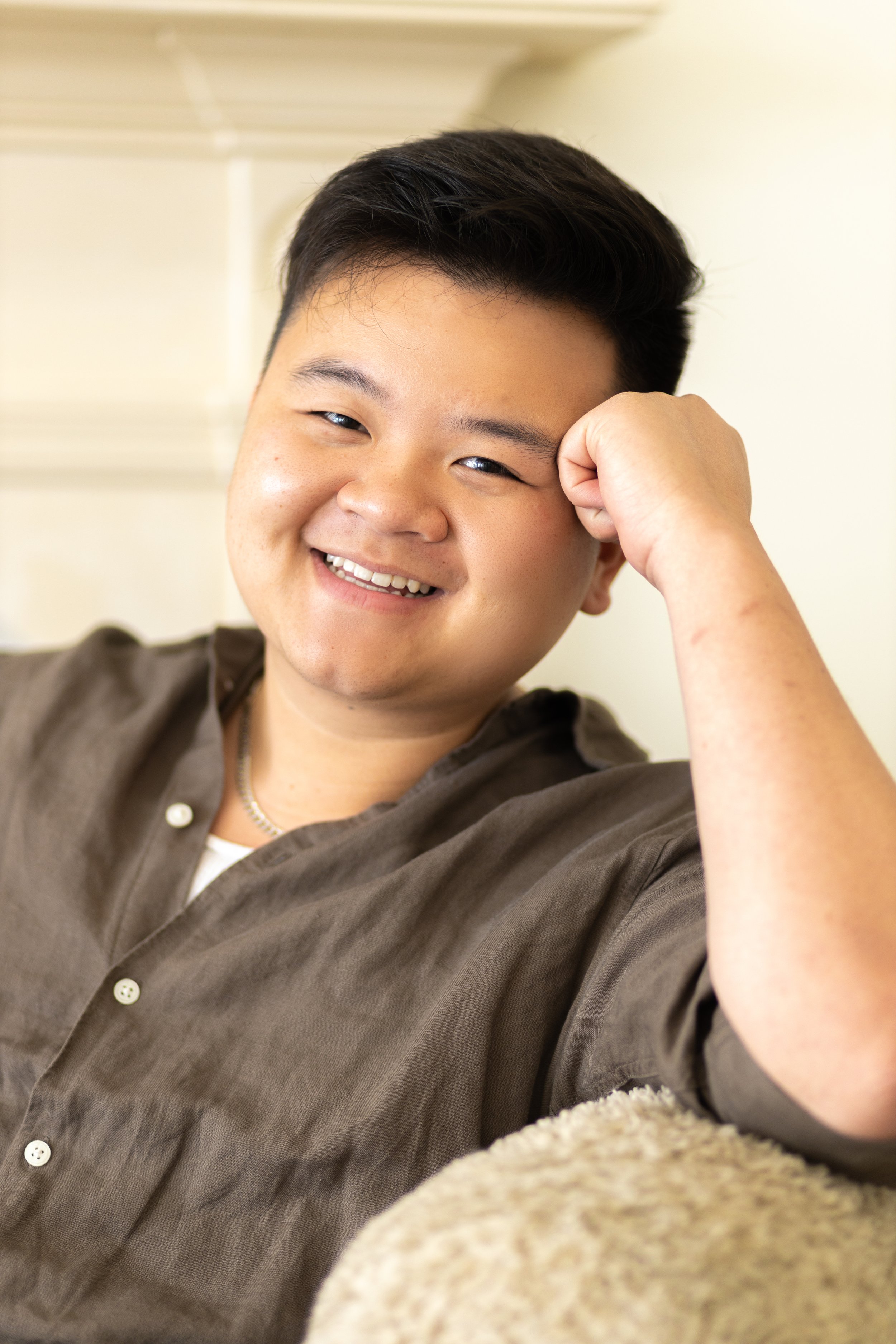 A young man with dark hair smiling and resting his head on his hand.