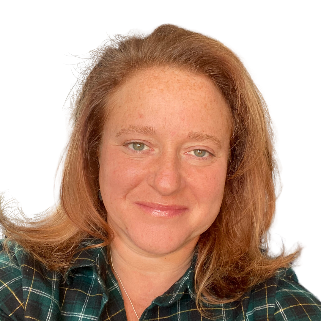 A woman with shoulder-length red hair and green eyes, wearing a green plaid shirt, smiling against a white background.