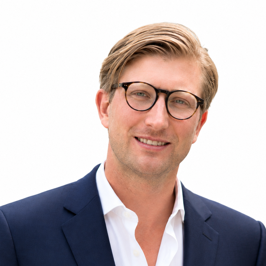 Professional man with blonde hair and glasses smiling, wearing a navy blazer and white shirt against a white background.