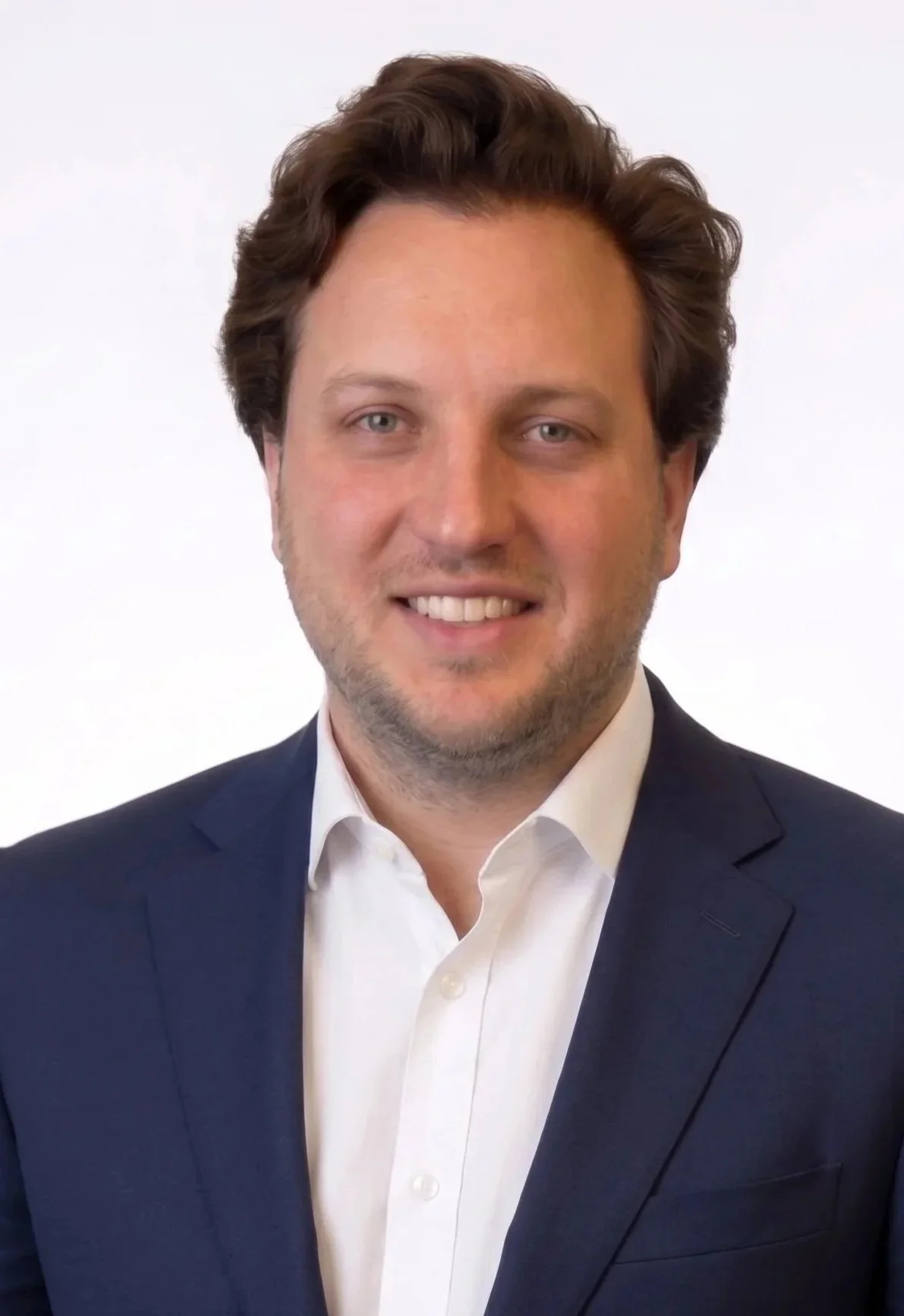 A man in a dark suit jacket and white dress shirt, smiling against a plain white background.