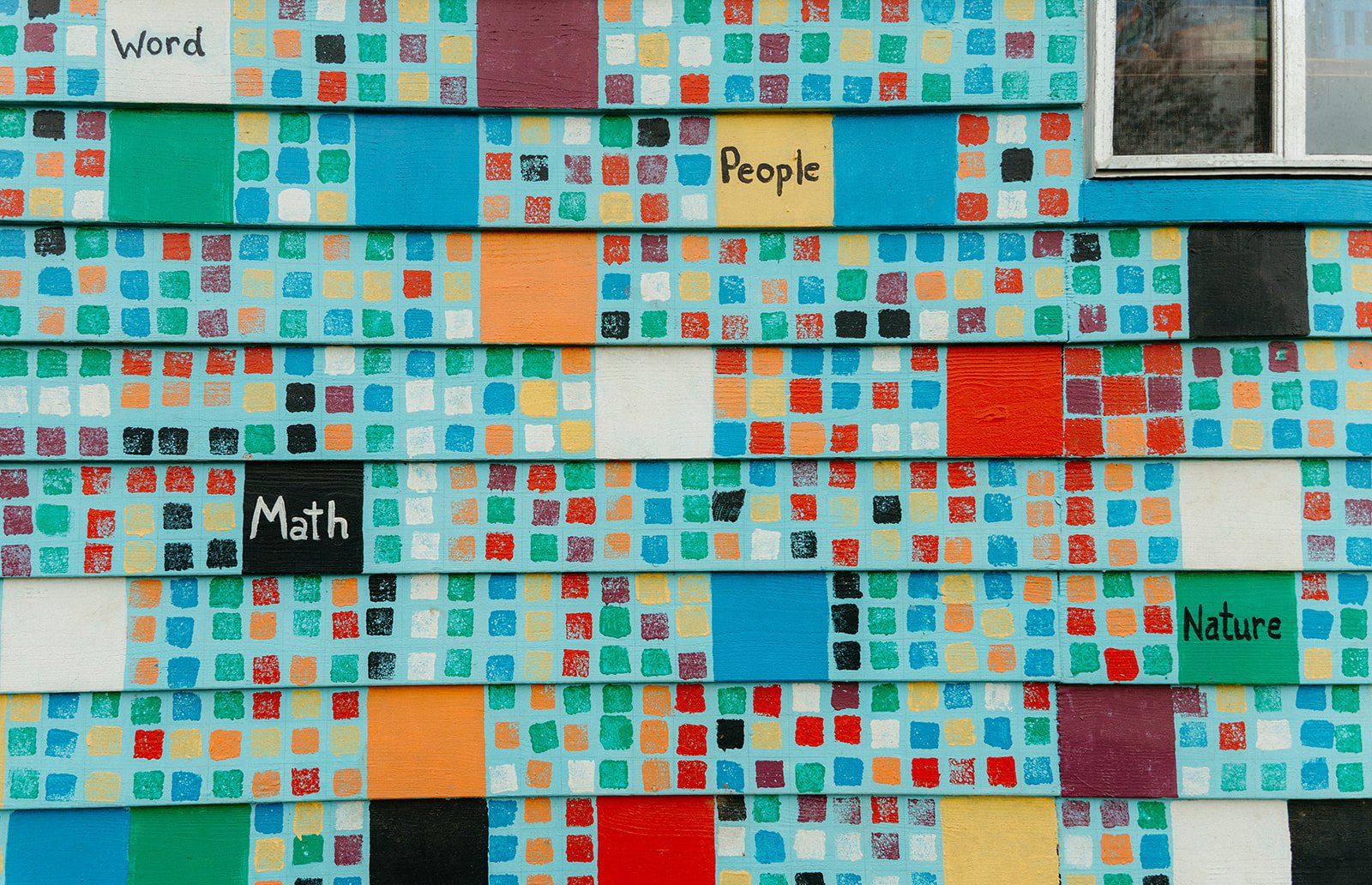 A colorful mural composed of small painted squares and larger painted sections featuring words like "Word," "People," "Math," and "Nature."