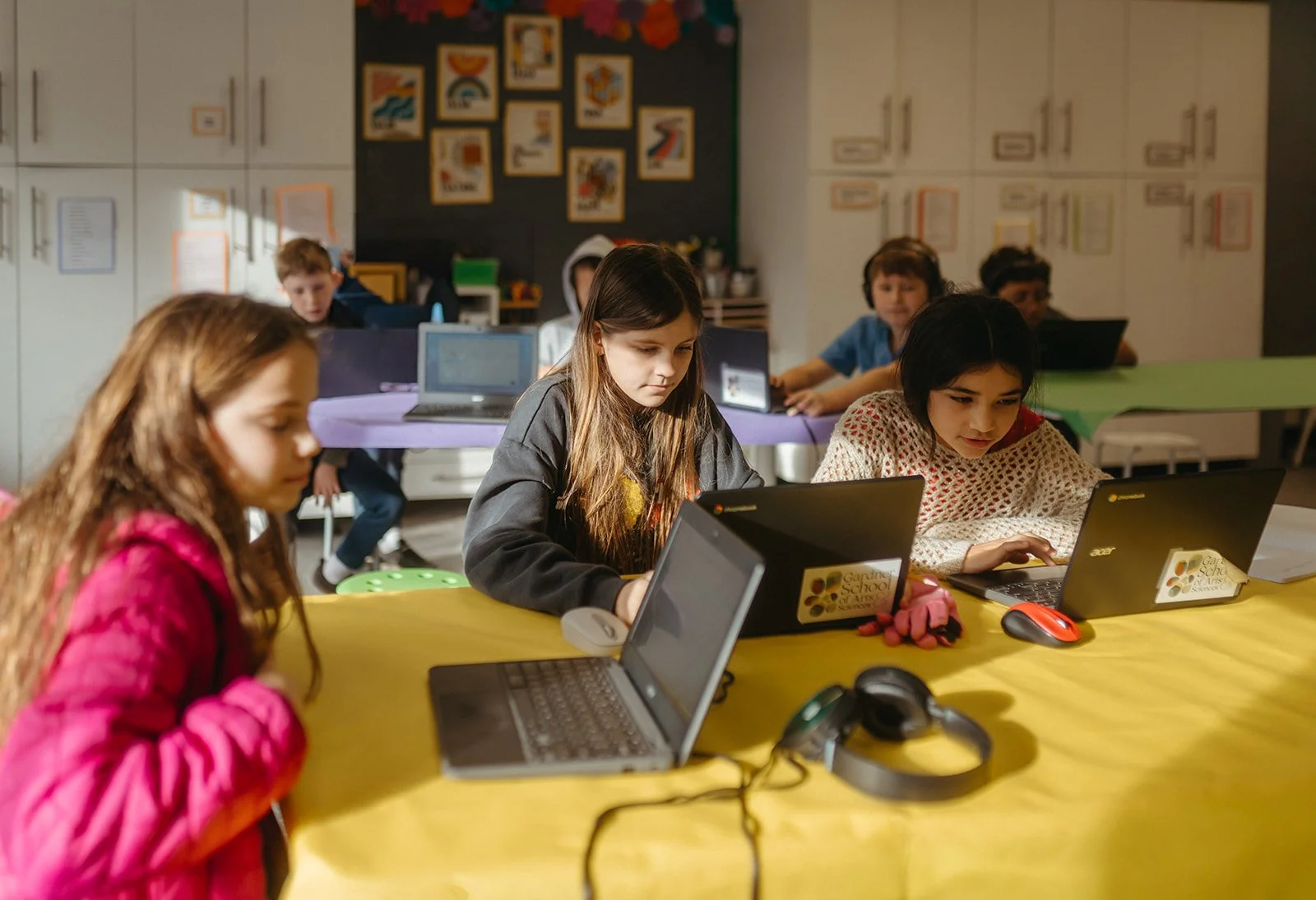 A classroom with young students working on laptops at colorful tables, engaging in educational activities.