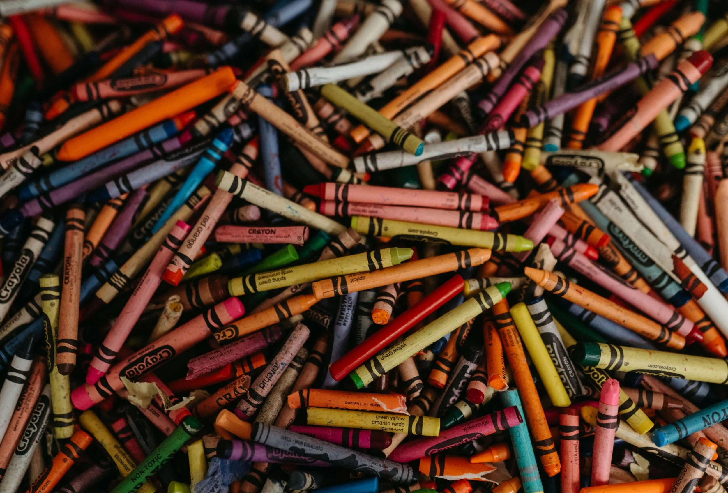 A close-up of a large pile of used colored crayons, some broken and scattered.