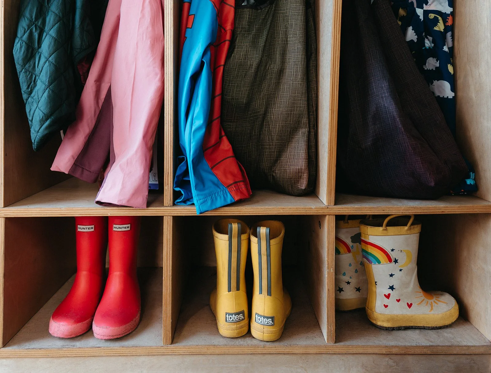 Cubby shelf with children's rain boots, jackets, and coats.