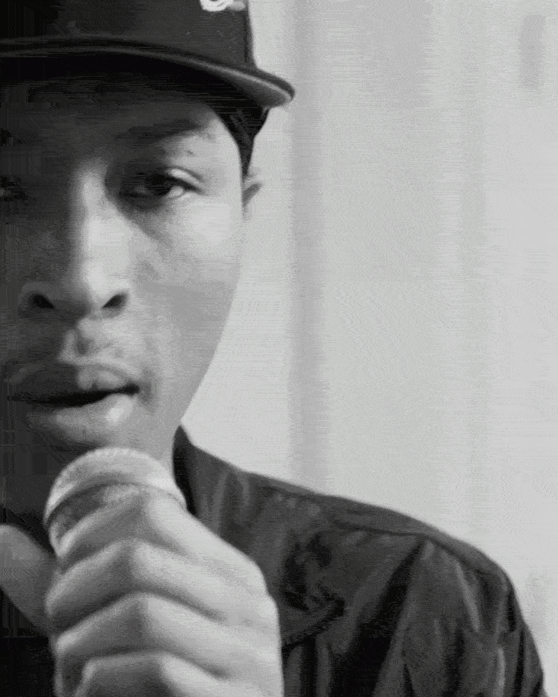 Close-up of a person wearing a police or military uniform and cap, holding a microphone close to their mouth, with a serious expression.