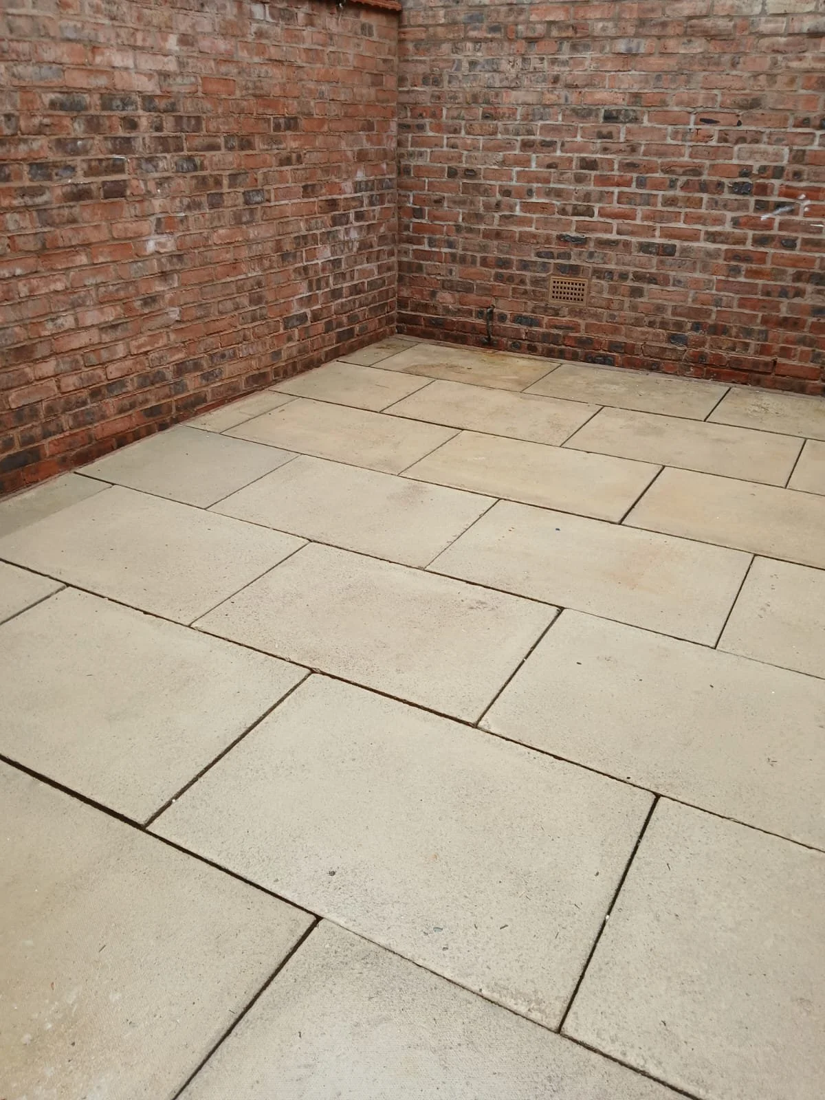 A corner of a red brick wall with beige tile flooring.