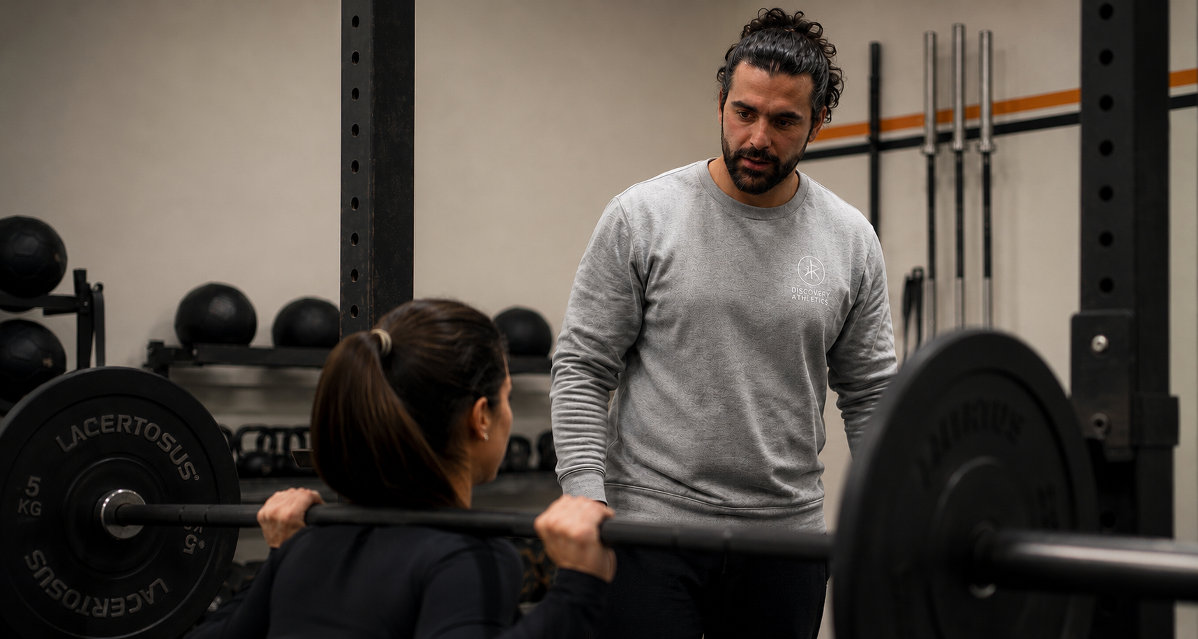 Un uomo che aiuta una donna a sollevare un bilanciere in palestra.