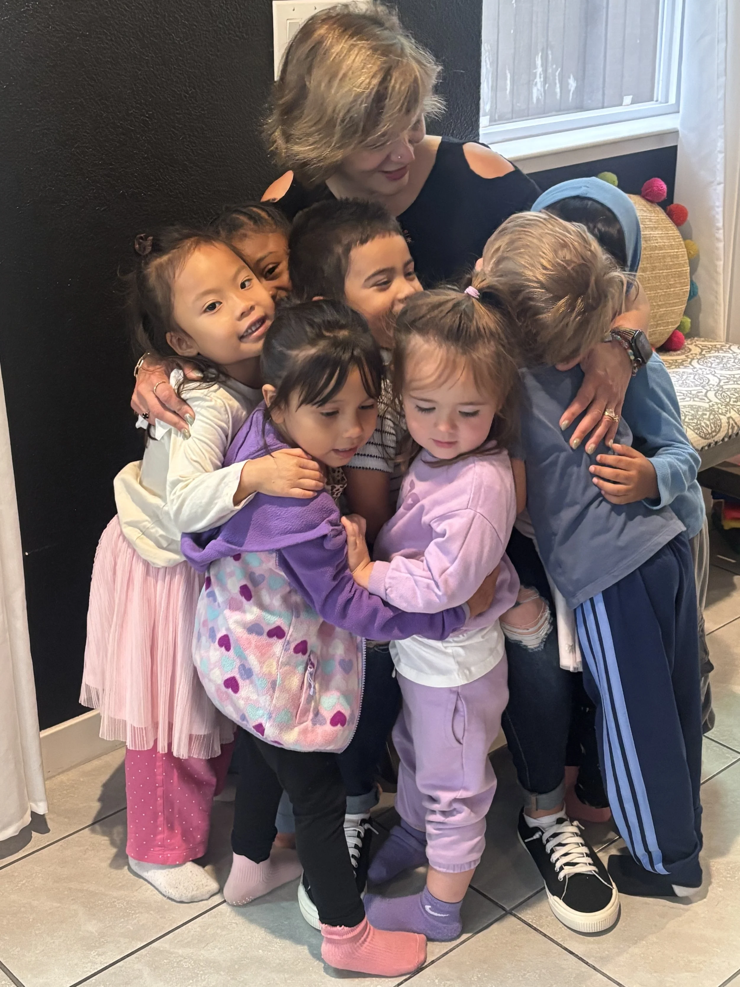 Caregiver sharing a group hug with preschool children in a nurturing home daycare and preschool environment in Sacramento