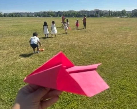 Preschool children flying handmade paper airplanes outdoors while exploring creativity, movement, and hands on learning at BabeeShark Preschool in Sacramento