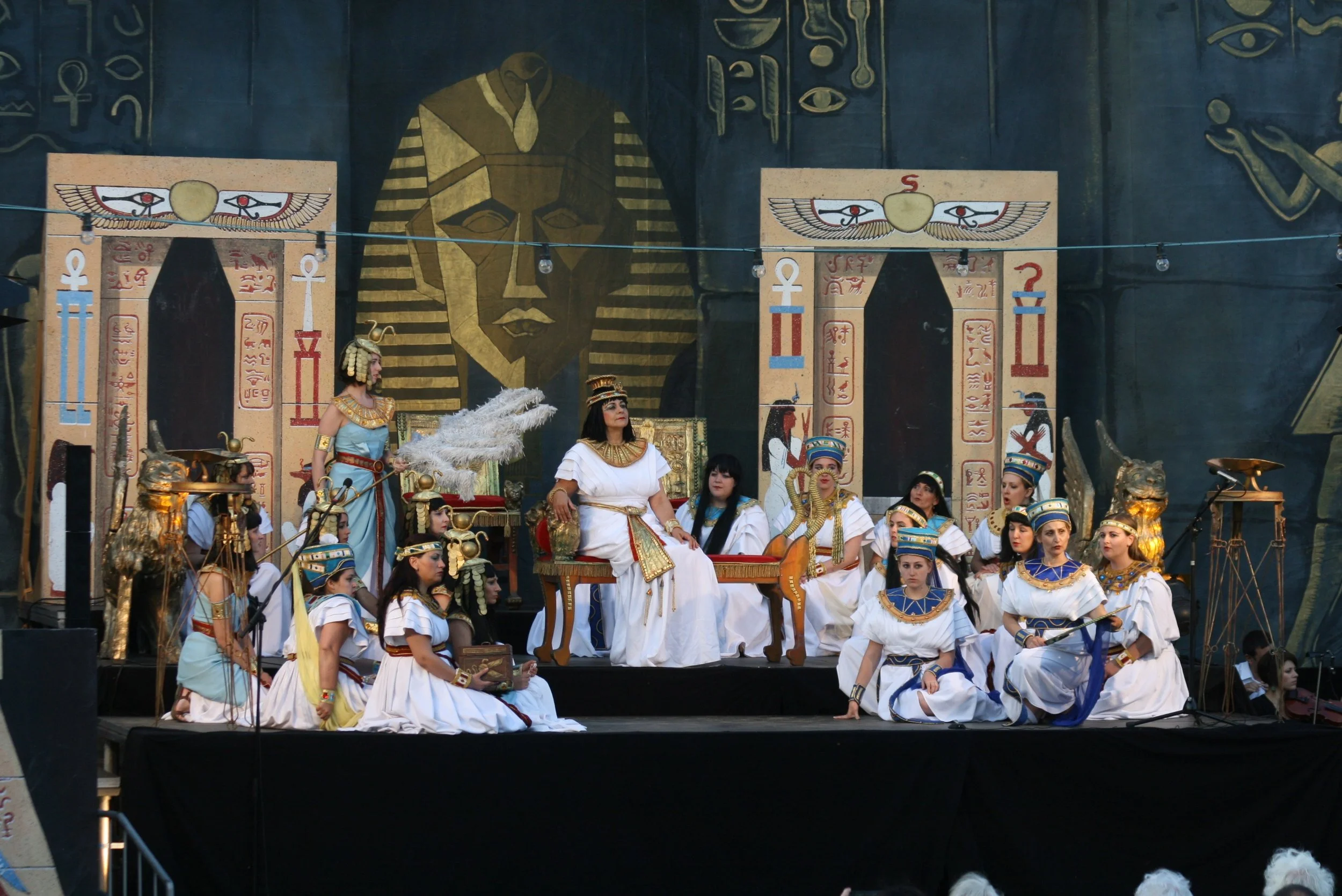 People dressed as ancient Egyptian pharaohs and gods participating in a theatrical performance with Egyptian-themed backdrop and props.