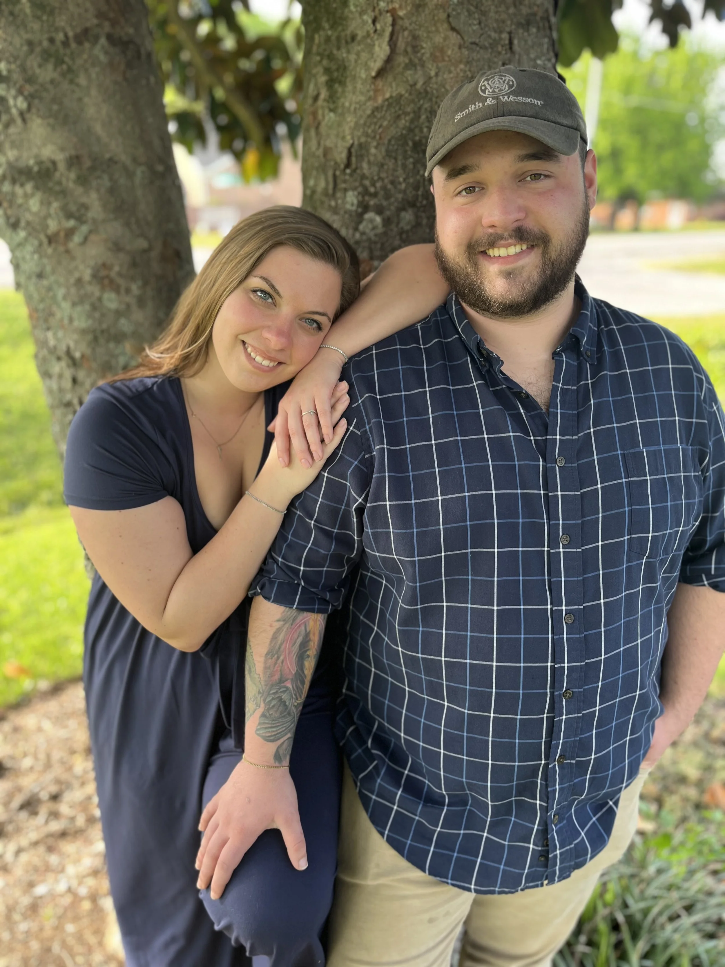 A woman and a man posing outdoors with their backs against a tree, smiling and looking at the camera. ready for Pressure washing and soft washing estimates in Chattanooga area