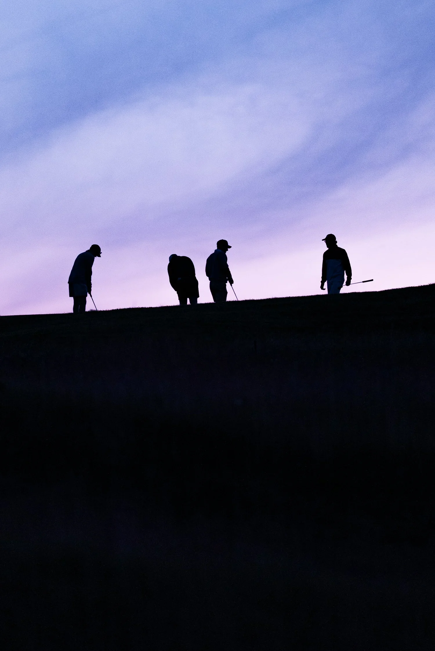 Four silhouettes of people on a hill at dusk, holding golf clubs, with a purple and blue sky in the background.