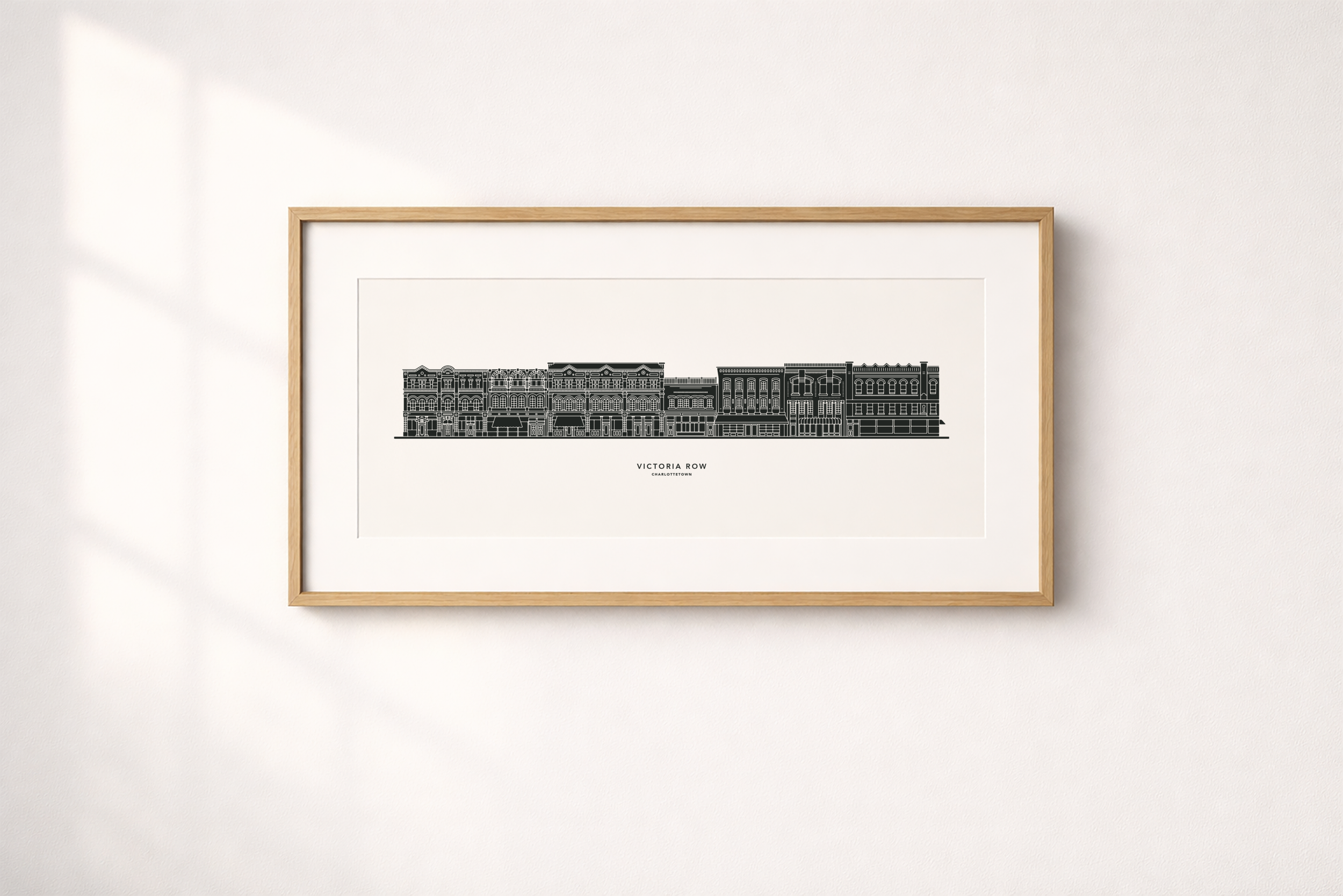 Framed black and white digital illustration of a cityscape titled Victoria Row Charlottetown, hanging on a white wall.