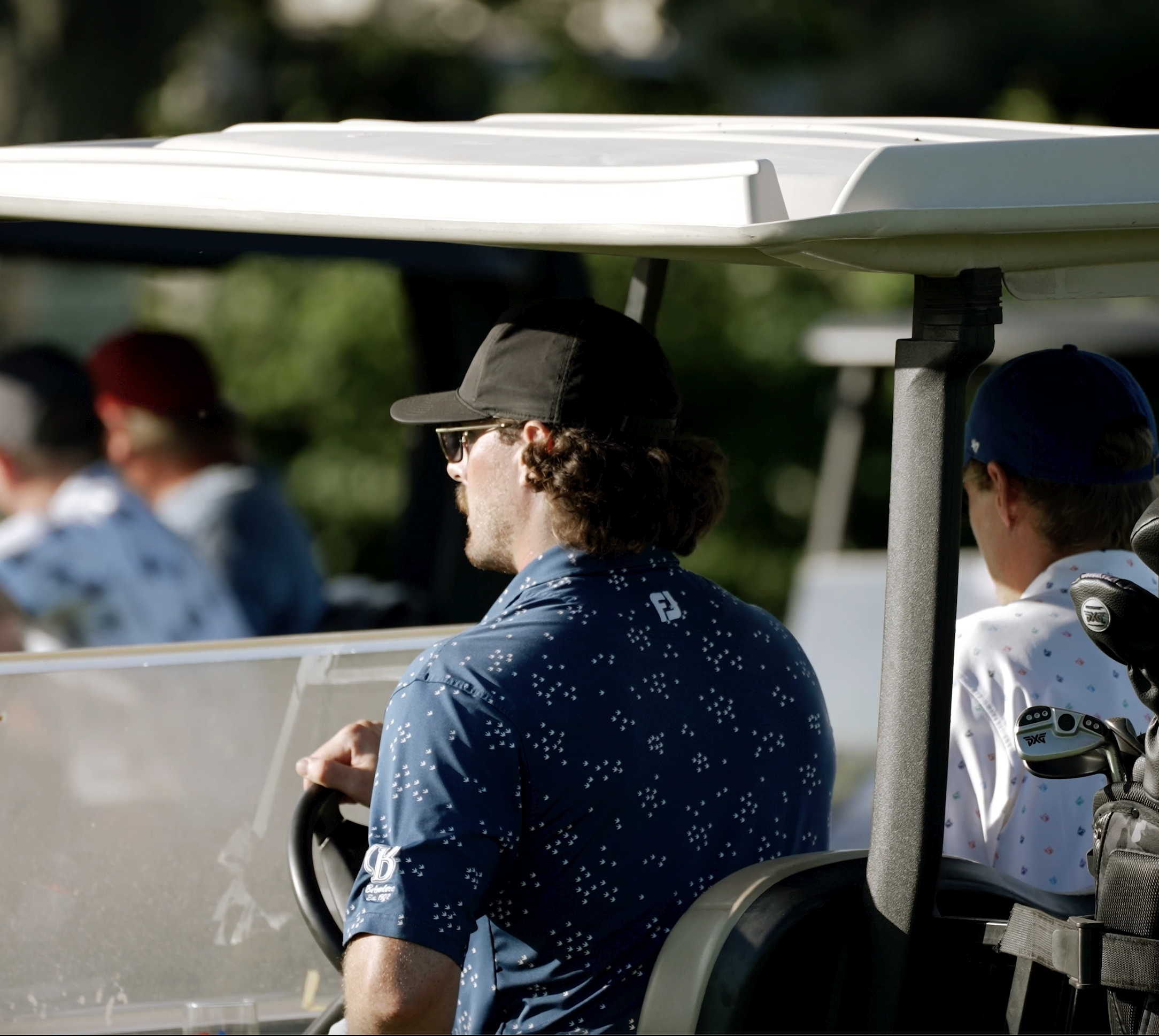 My Biggest Fan Foundation Charity Golf Tournament. People on a golf cart wearing hats and sunglasses, with golf clubs and equipment visible.