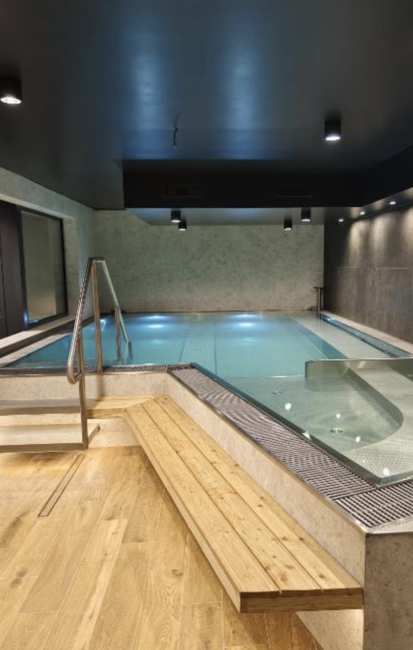 Indoor swimming pool area with wooden benches, metal handrails, and modern ceiling lighting.