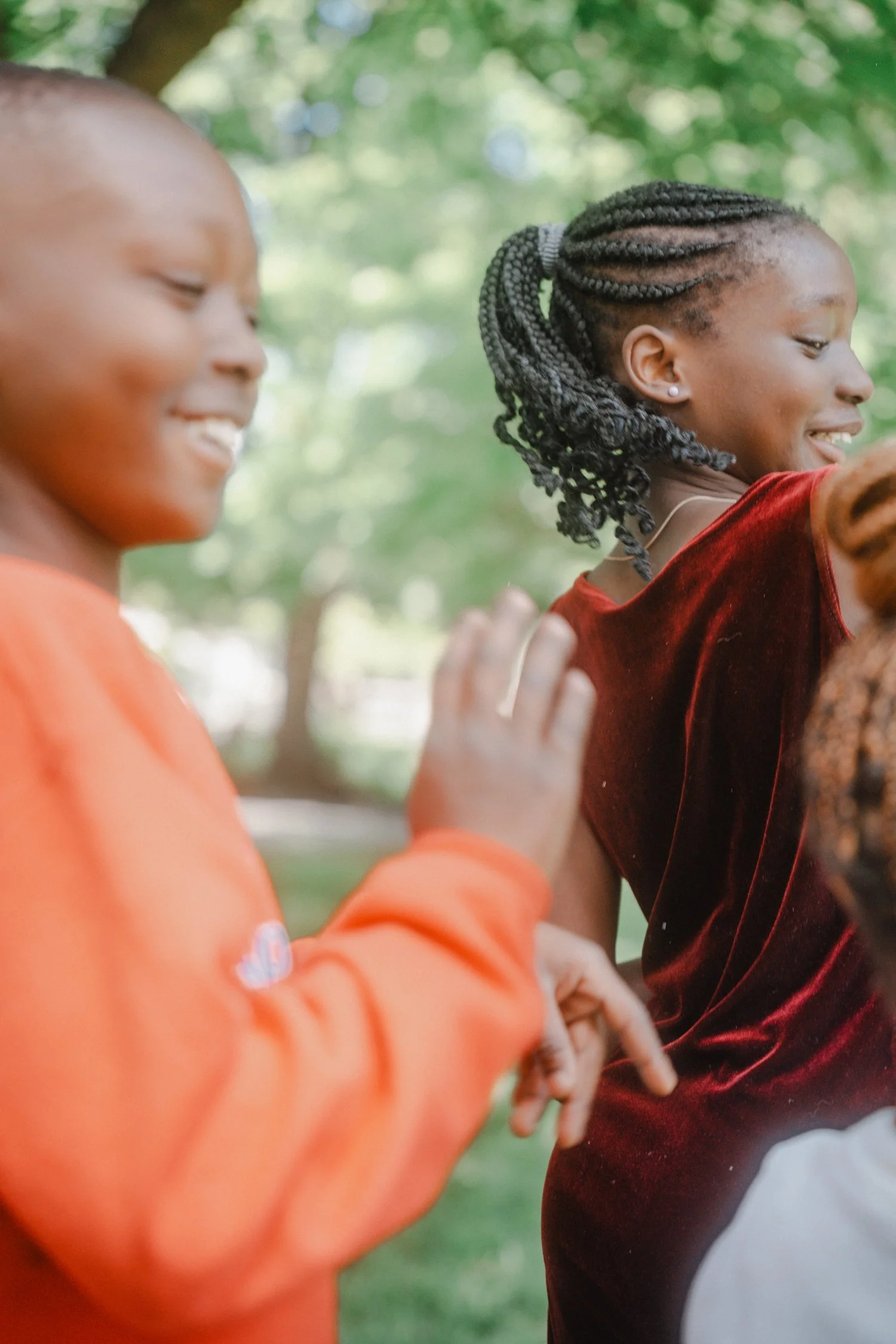 Close-up of two children smiling and playing outdoors, with greens and sunlight in the blurred background.