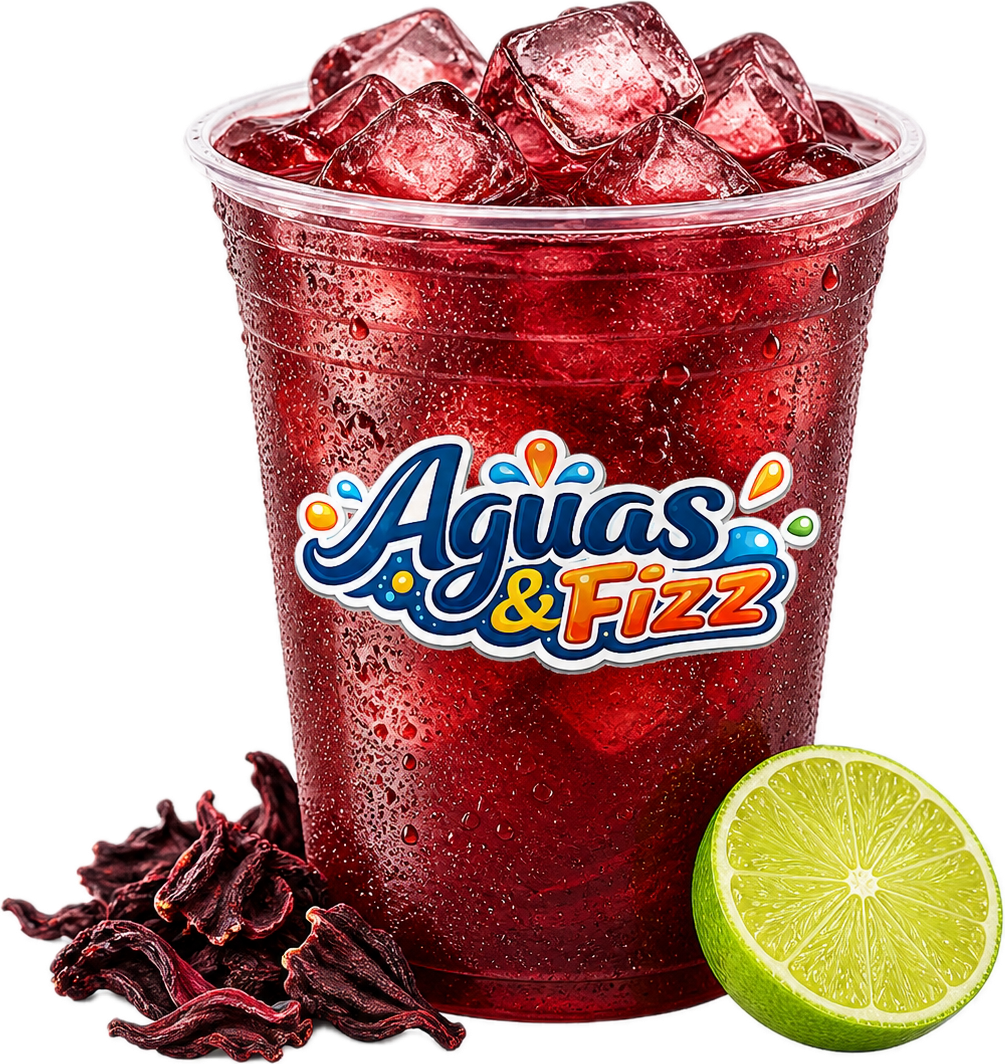 A plastic cup filled with red soda and ice cubes. There is a sliced lime and dried hibiscus flowers next to the cup.