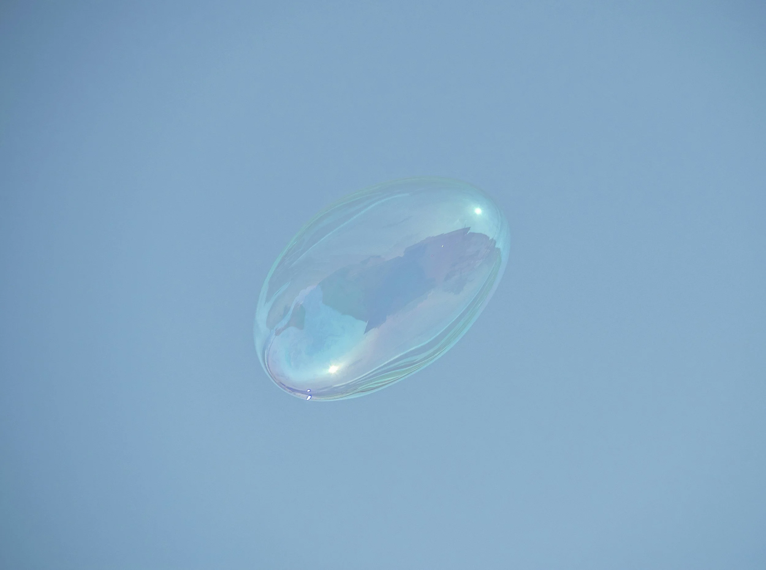 A single soap bubble floating against a bright blue sky.