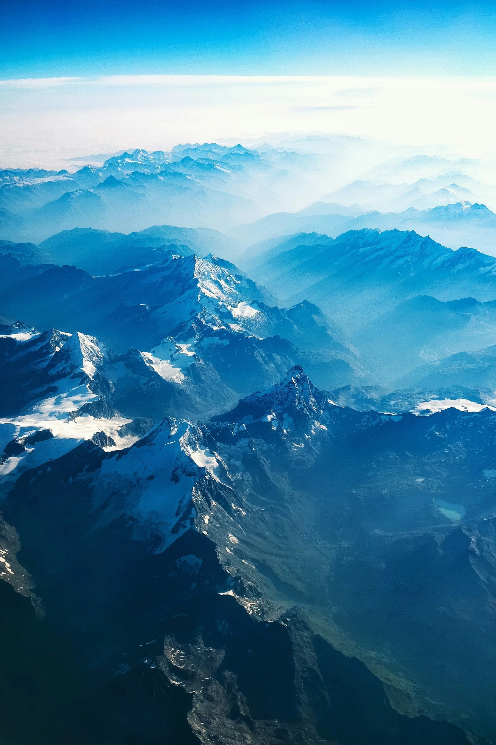 Aerial view of snow-capped mountain range with mist and clouds in the distance.